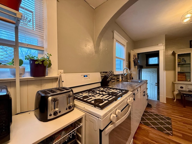 kitchen featuring plenty of natural light, white gas range oven, a sink, and wood finished floors