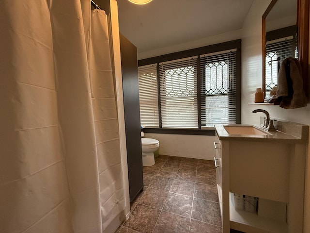 full bath with toilet, stone finish flooring, and vanity