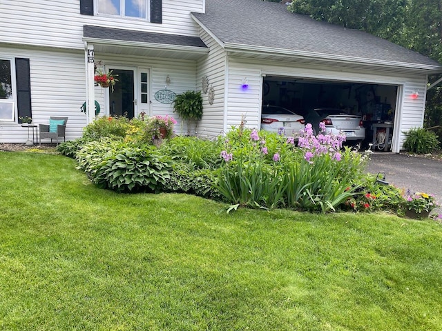 exterior space with a yard, an attached garage, driveway, and roof with shingles