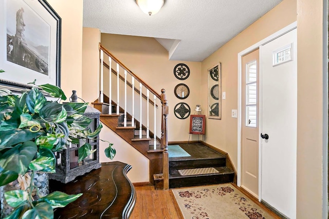 foyer with stairs, a textured ceiling, baseboards, and wood finished floors