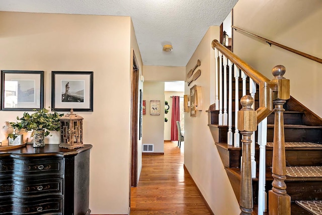 hall with stairway, a textured ceiling, wood finished floors, and visible vents