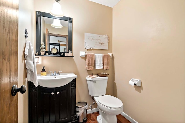 half bath with vanity, baseboards, toilet, and wood finished floors