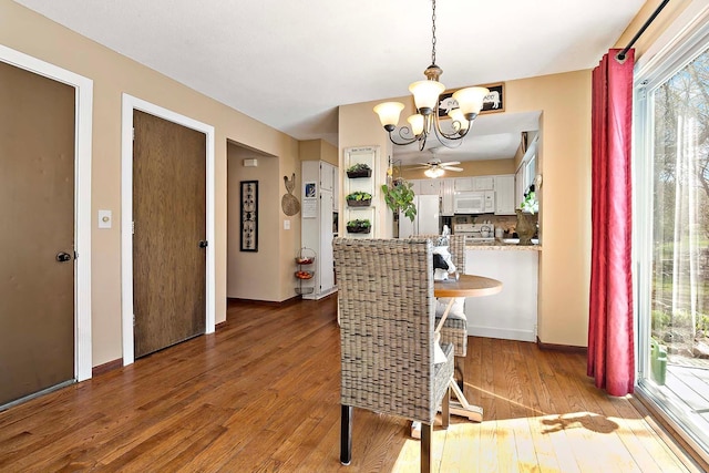 dining room featuring light wood-type flooring, baseboards, and ceiling fan with notable chandelier