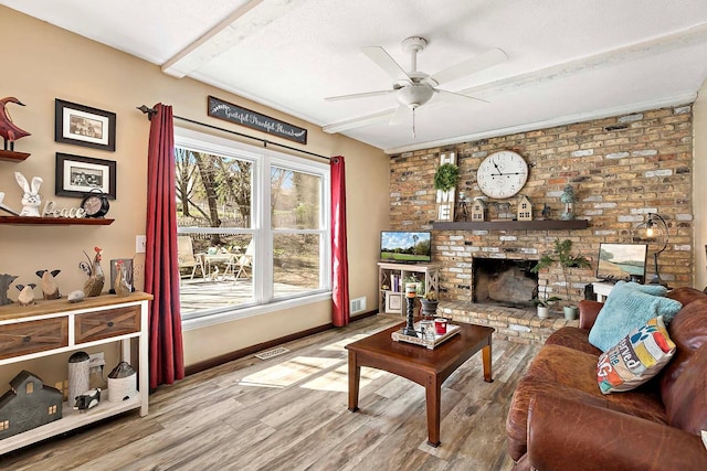 living area with a brick fireplace, a ceiling fan, visible vents, and wood finished floors