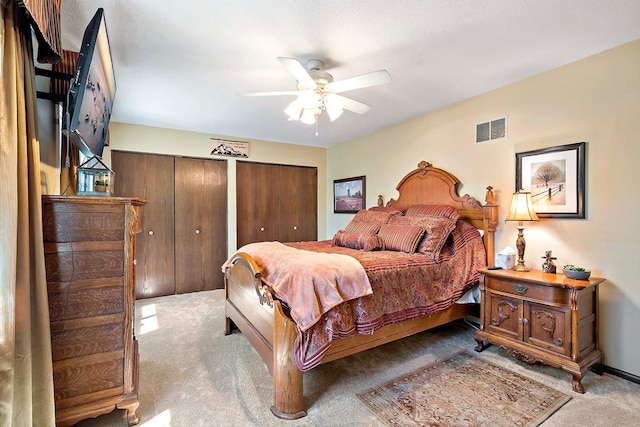 carpeted bedroom with visible vents, multiple closets, and ceiling fan