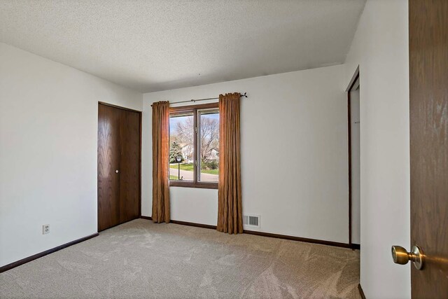 carpeted empty room with visible vents, a textured ceiling, and baseboards