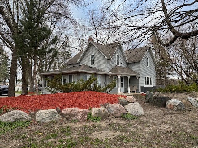 farmhouse inspired home with a shingled roof, a chimney, and a porch