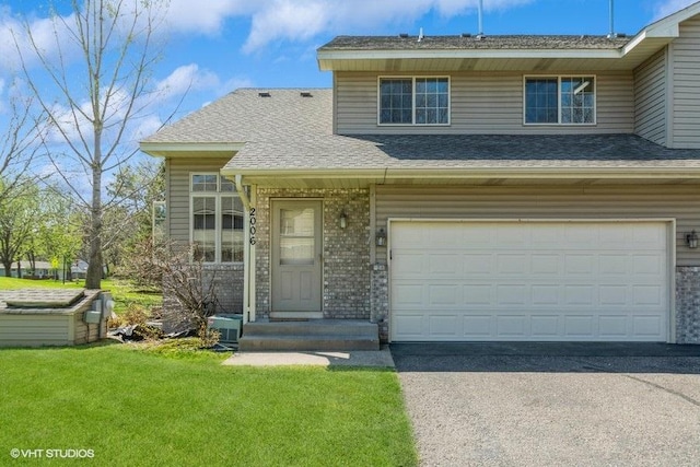 view of front of property with roof with shingles, an attached garage, driveway, and a front lawn