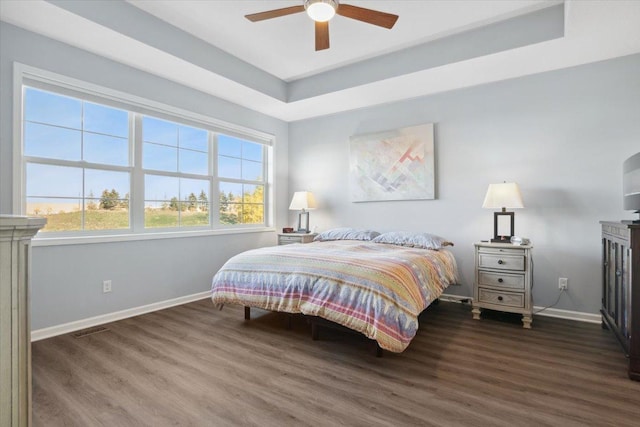 bedroom featuring a raised ceiling, a ceiling fan, visible vents, baseboards, and wood finished floors