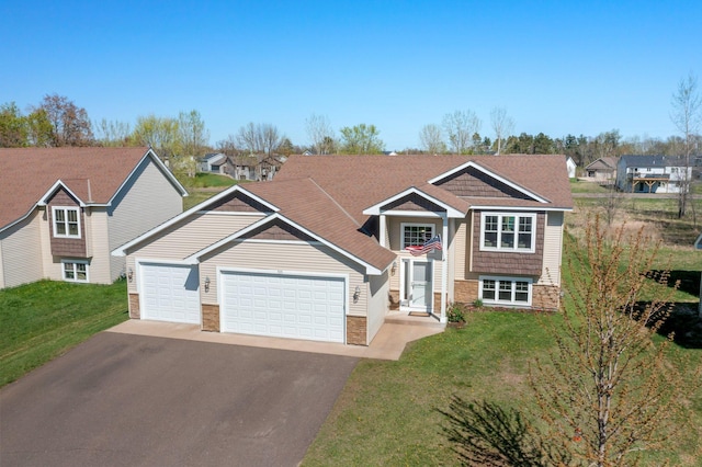 raised ranch featuring a front yard, stone siding, a garage, and aphalt driveway