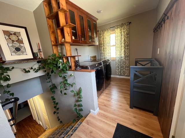 kitchen with brown cabinetry, baseboards, light wood-type flooring, washing machine and dryer, and glass insert cabinets