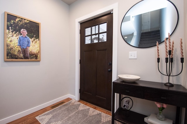 foyer entrance featuring baseboards, wood finished floors, and visible vents