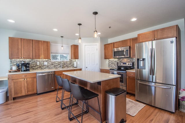 kitchen with decorative backsplash, appliances with stainless steel finishes, light countertops, light wood finished floors, and a breakfast bar