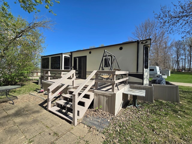 rear view of property featuring a deck, stucco siding, a sunroom, and a patio