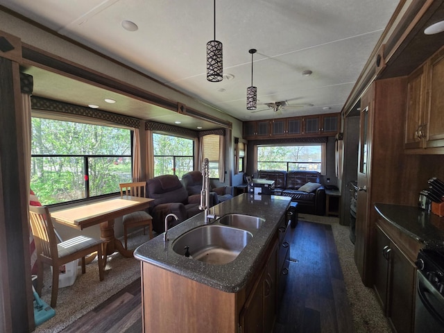 kitchen featuring a sink, dark stone counters, a kitchen island with sink, a wealth of natural light, and range
