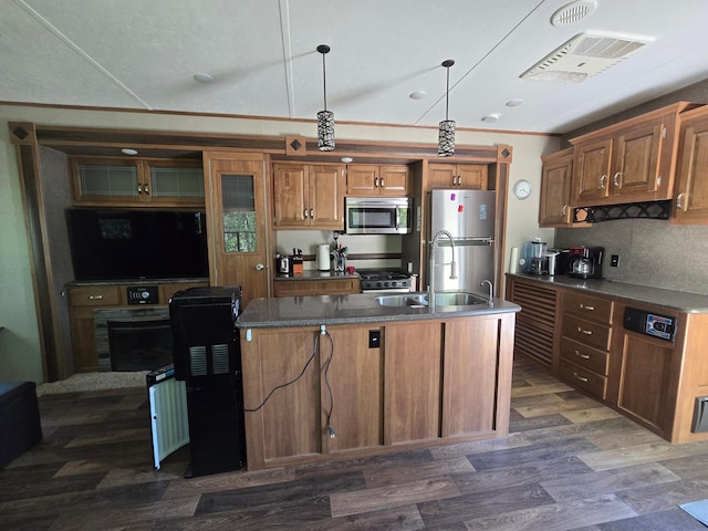 kitchen featuring a sink, stainless steel appliances, brown cabinetry, a center island with sink, and dark wood-style flooring