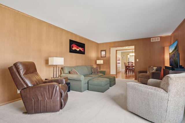 carpeted living area with wood walls, visible vents, and an inviting chandelier