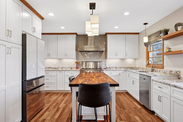 kitchen with butcher block countertops, wall chimney exhaust hood, a sink, light wood finished floors, and stainless steel appliances
