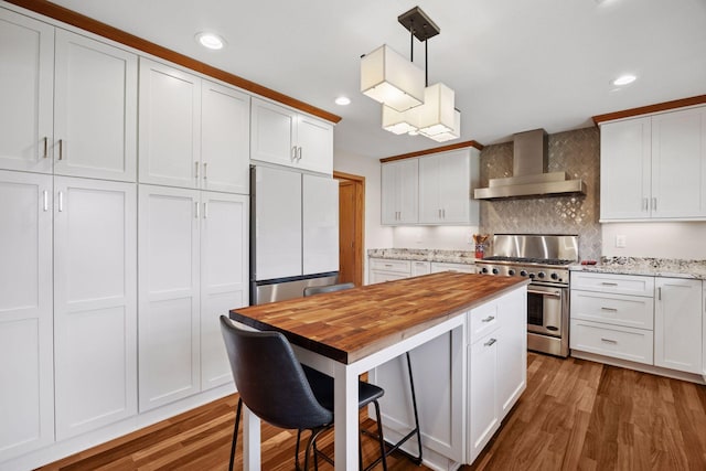kitchen featuring high end stove, wall chimney exhaust hood, built in refrigerator, white cabinets, and butcher block countertops