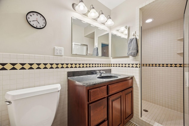 bathroom with vanity, wainscoting, toilet, tile walls, and a tile shower