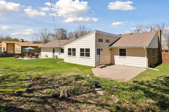 rear view of property with fence, a patio, a yard, and roof with shingles