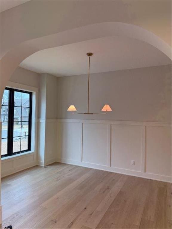 unfurnished dining area with a decorative wall, light wood-type flooring, a wainscoted wall, and arched walkways