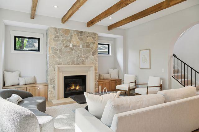 9399 Eagle Ridge Way, Chanhassen, MN 55317 - living room with a stone fireplace, beamed ceiling, stairway, arched walkways, and wood finished floors