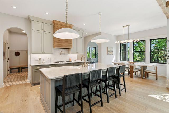 9399 Eagle Ridge Way, Chanhassen, MN 55317 - kitchen with arched walkways, light wood-type flooring, stovetop, an island with sink, and backsplash