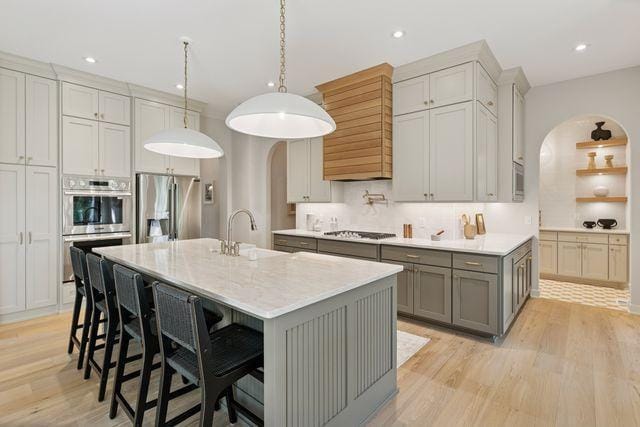 9399 Eagle Ridge Way, Chanhassen, MN 55317 - kitchen featuring arched walkways, gray cabinets, stainless steel appliances, custom range hood, and light wood-type flooring