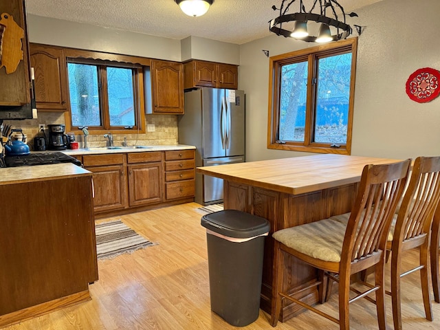 kitchen with light wood finished floors, a kitchen bar, freestanding refrigerator, wood counters, and backsplash