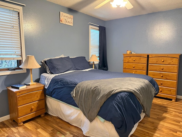 bedroom with a textured ceiling, wood finished floors, ceiling fan, and a textured wall