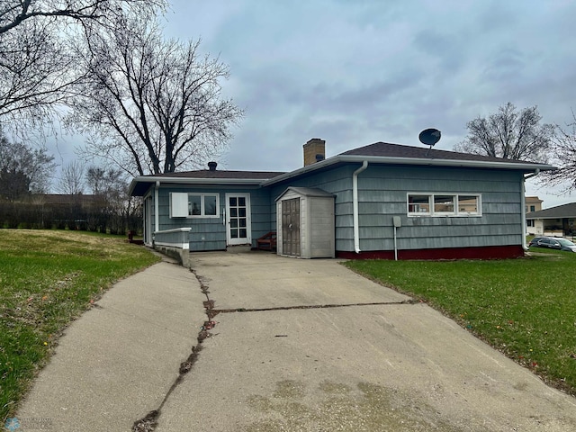 rear view of property featuring a yard, a chimney, and concrete driveway