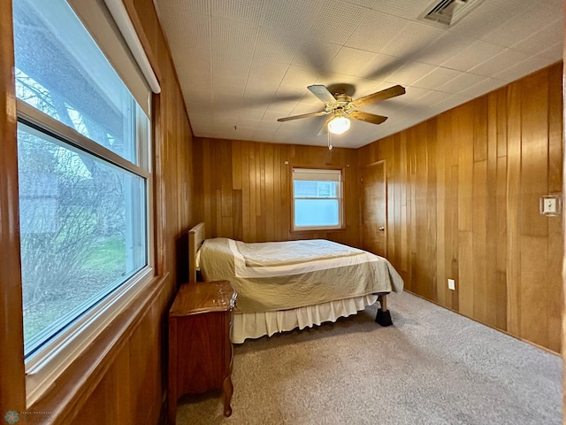 carpeted bedroom with visible vents, ceiling fan, and wooden walls