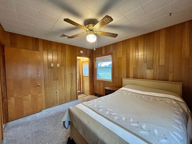 bedroom featuring wooden walls, a ceiling fan, visible vents, and carpet