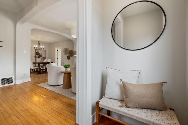 living area featuring visible vents, arched walkways, baseboards, an inviting chandelier, and hardwood / wood-style floors