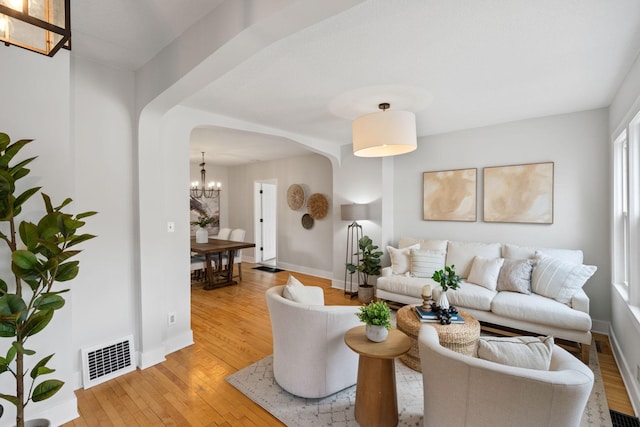 living area featuring visible vents, arched walkways, baseboards, a notable chandelier, and light wood-style flooring