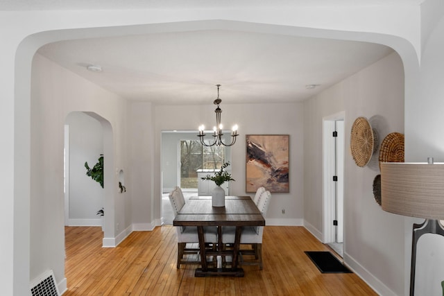 dining space with an inviting chandelier, arched walkways, light wood-style floors, and visible vents