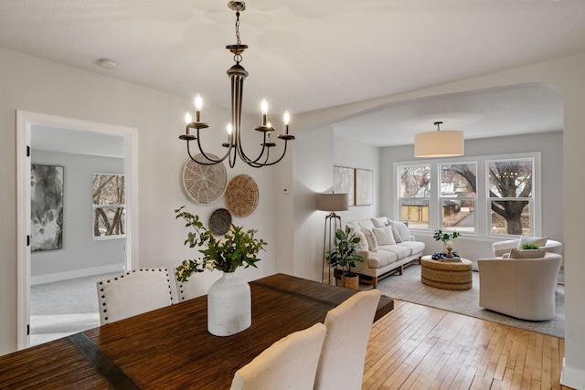 dining area with an inviting chandelier, arched walkways, and light wood-type flooring