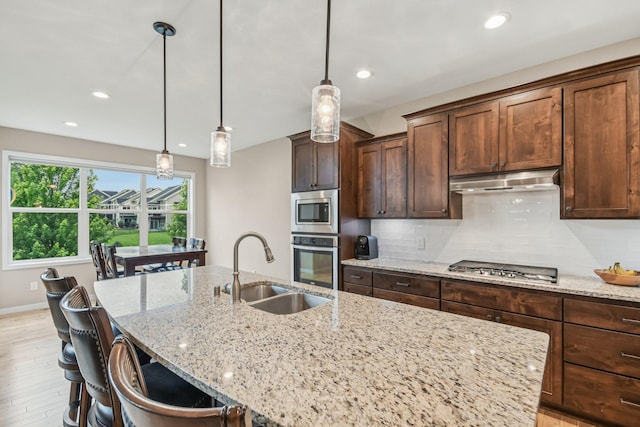 3623 Cove Point Cir NW, Prior Lake, MN 55372 - kitchen featuring stainless steel appliances, a kitchen island with sink, decorative backsplash, light wood-type flooring, and light stone countertops
