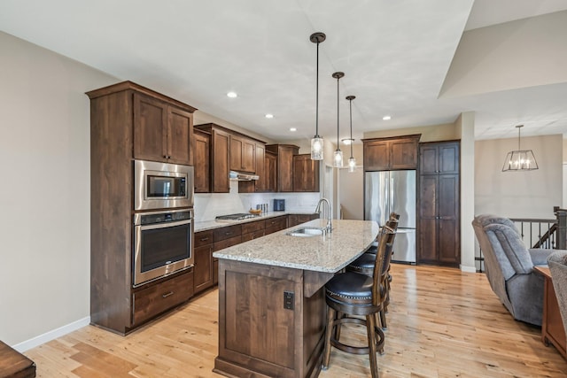 3623 Cove Point Cir NW, Prior Lake, MN 55372 - kitchen with appliances with stainless steel finishes, under cabinet range hood, light wood-style floors, light stone countertops, and recessed lighting