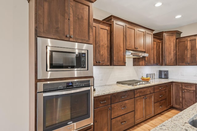 3623 Cove Point Cir NW, Prior Lake, MN 55372 - kitchen featuring appliances with stainless steel finishes, under cabinet range hood, light stone counters, decorative backsplash, and light wood-style floors