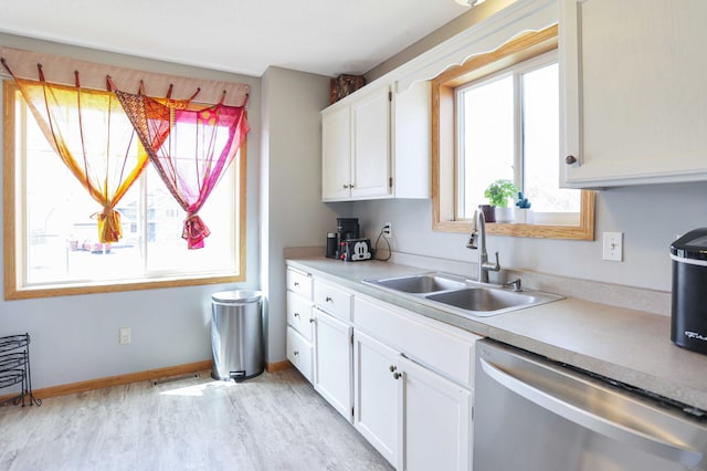 kitchen featuring stainless steel dishwasher, light wood-style floors, light countertops, a sink, and white cabinetry