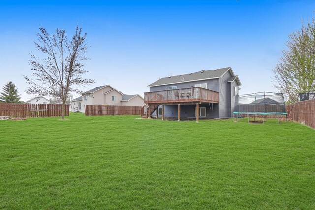 back of house with a wooden deck, a trampoline, a fenced backyard, a lawn, and stairs