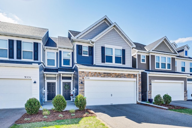 multi unit property with stone siding, aphalt driveway, and an attached garage