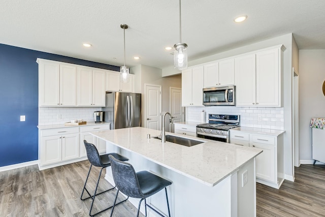 kitchen with baseboards, an island with sink, appliances with stainless steel finishes, and a sink