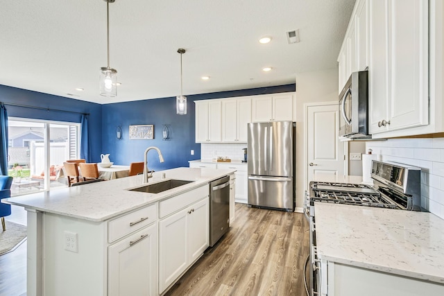 kitchen featuring light wood-style flooring, a sink, stainless steel appliances, white cabinets, and tasteful backsplash