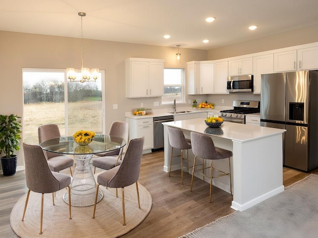 kitchen featuring a kitchen island, appliances with stainless steel finishes, a sink, white cabinets, and an inviting chandelier