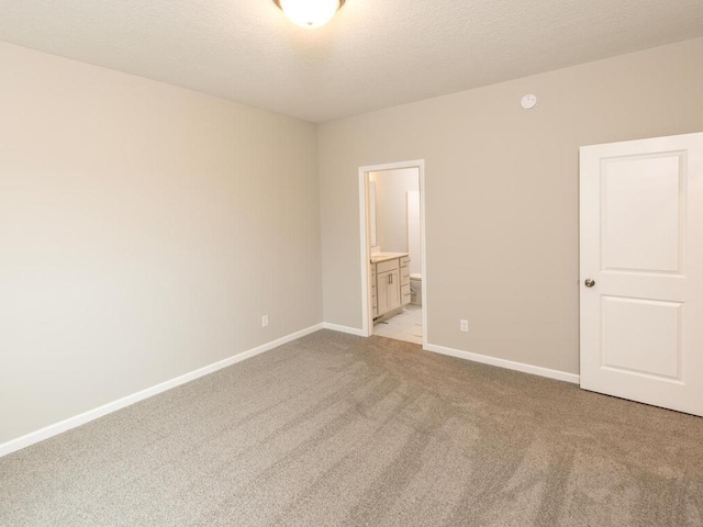 unfurnished bedroom with baseboards, ensuite bath, a textured ceiling, and light colored carpet