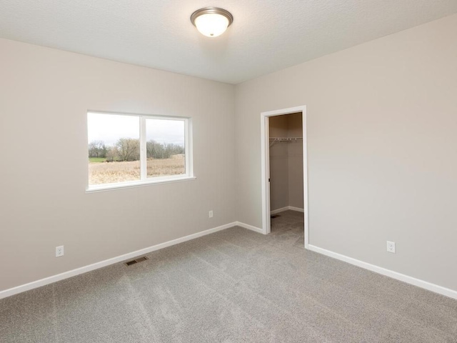 unfurnished bedroom featuring a walk in closet, visible vents, carpet floors, baseboards, and a closet