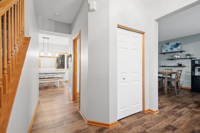 hall featuring stairs, baseboards, a notable chandelier, and wood finished floors